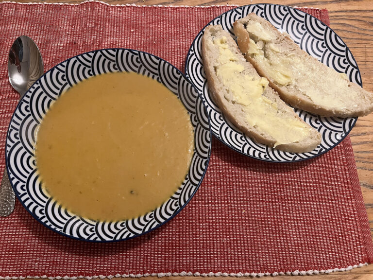 A bowl of sweet potato soup with homemade bread and butter